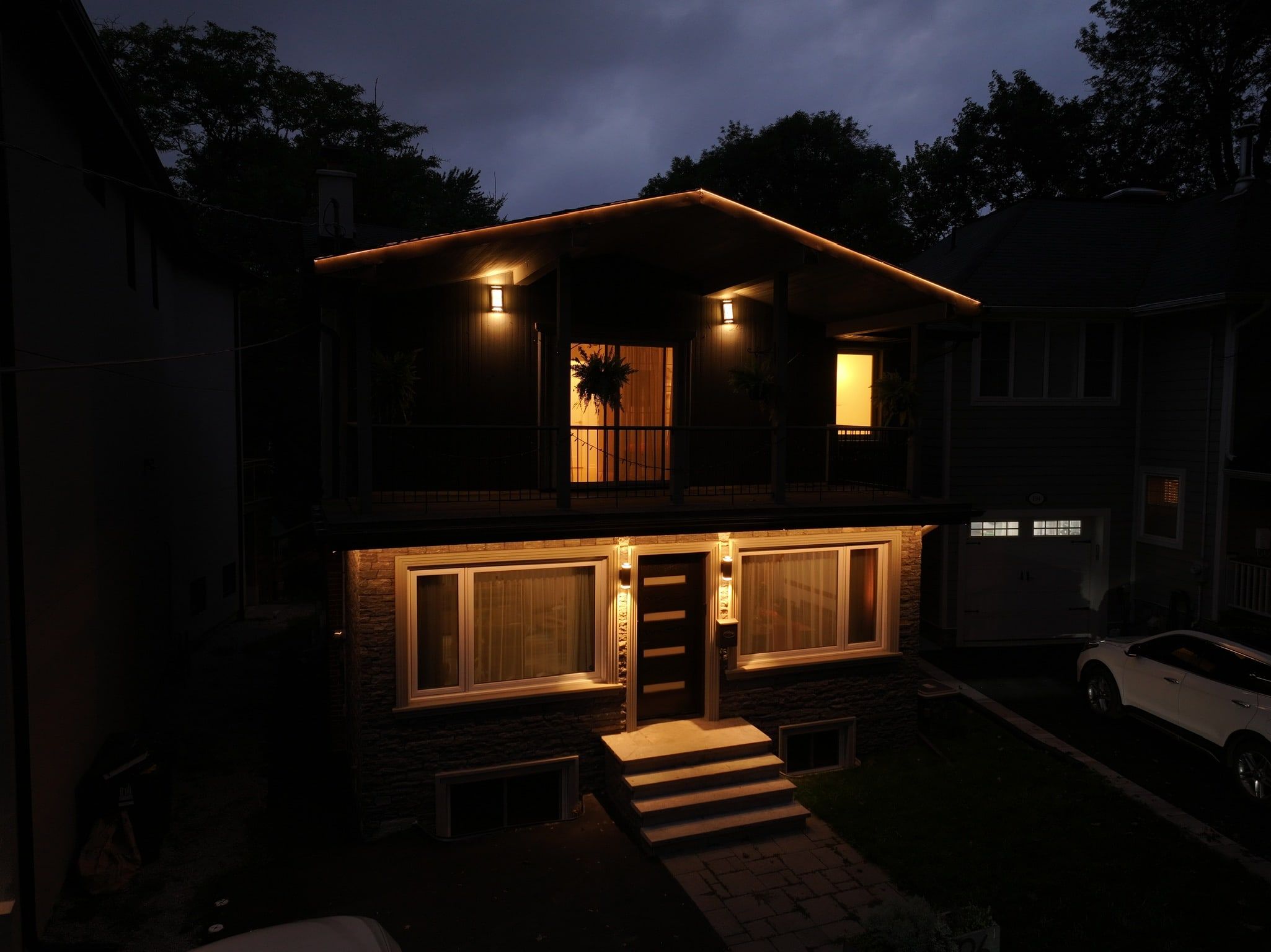 A two-storey gabled house at night with a warm light line along the roof edges and porch roof.