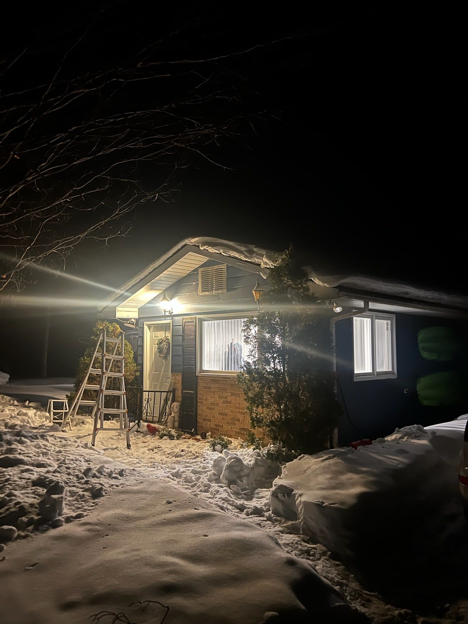A bungalow at night in snow with a warm light line along the eaves and gable.