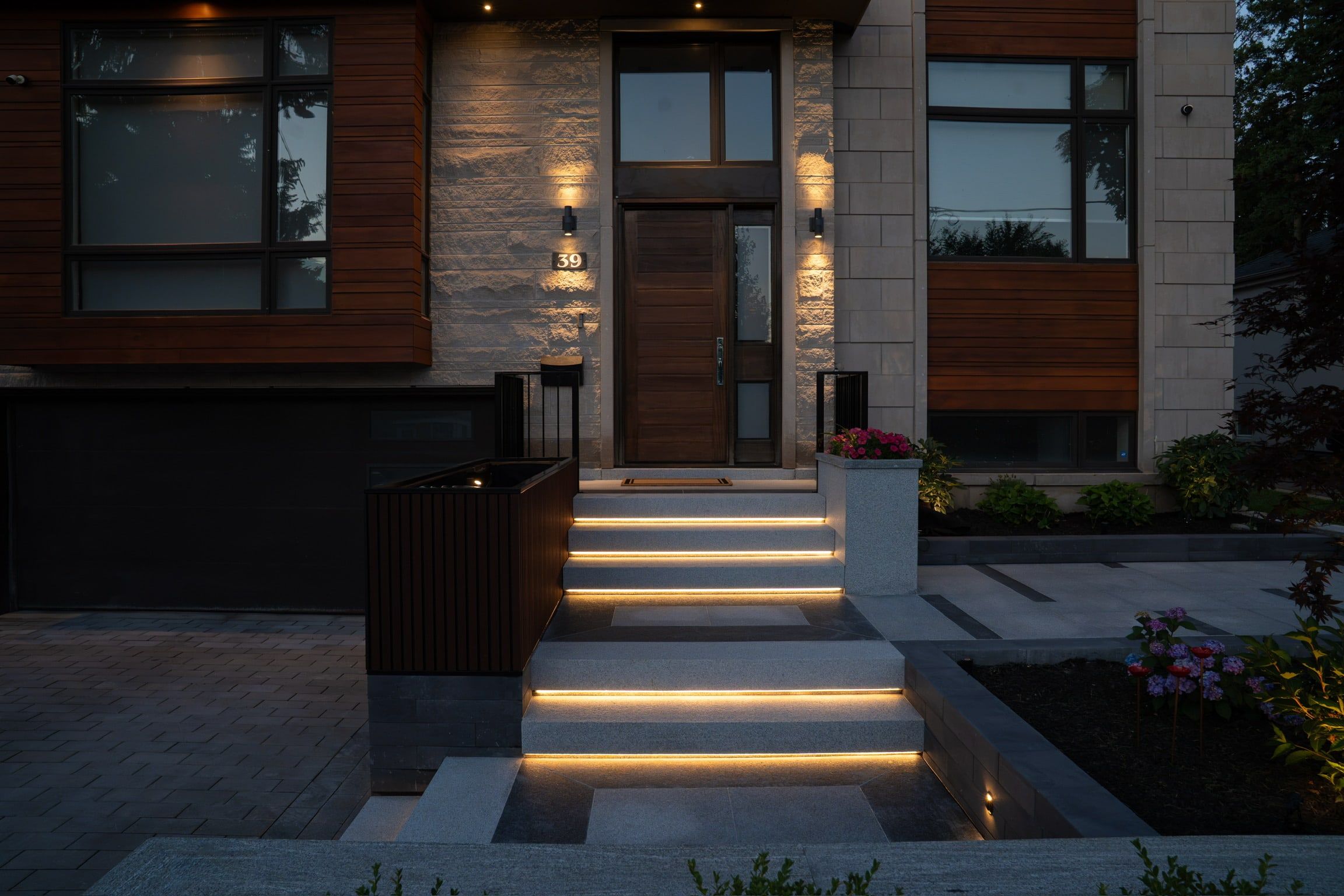 The entry at dusk: lit granite steps below a cream stone wall and wood-clad facade.