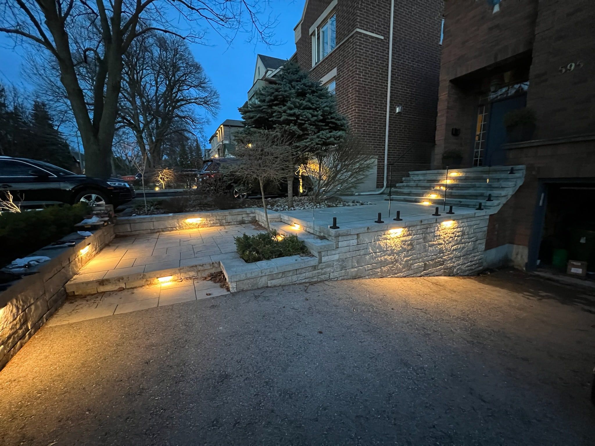 Multi-level stone front steps and terrace walls at dusk, with warm light under each step edge and wall cap.