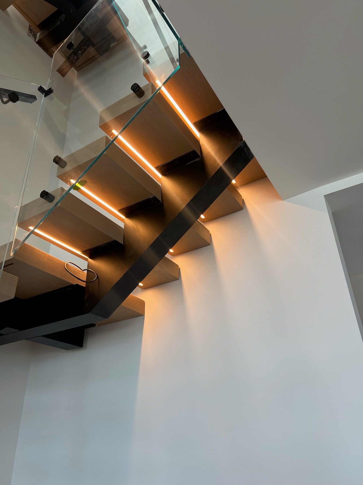 Looking up the floating staircase; warm light under each tread washes the wall.