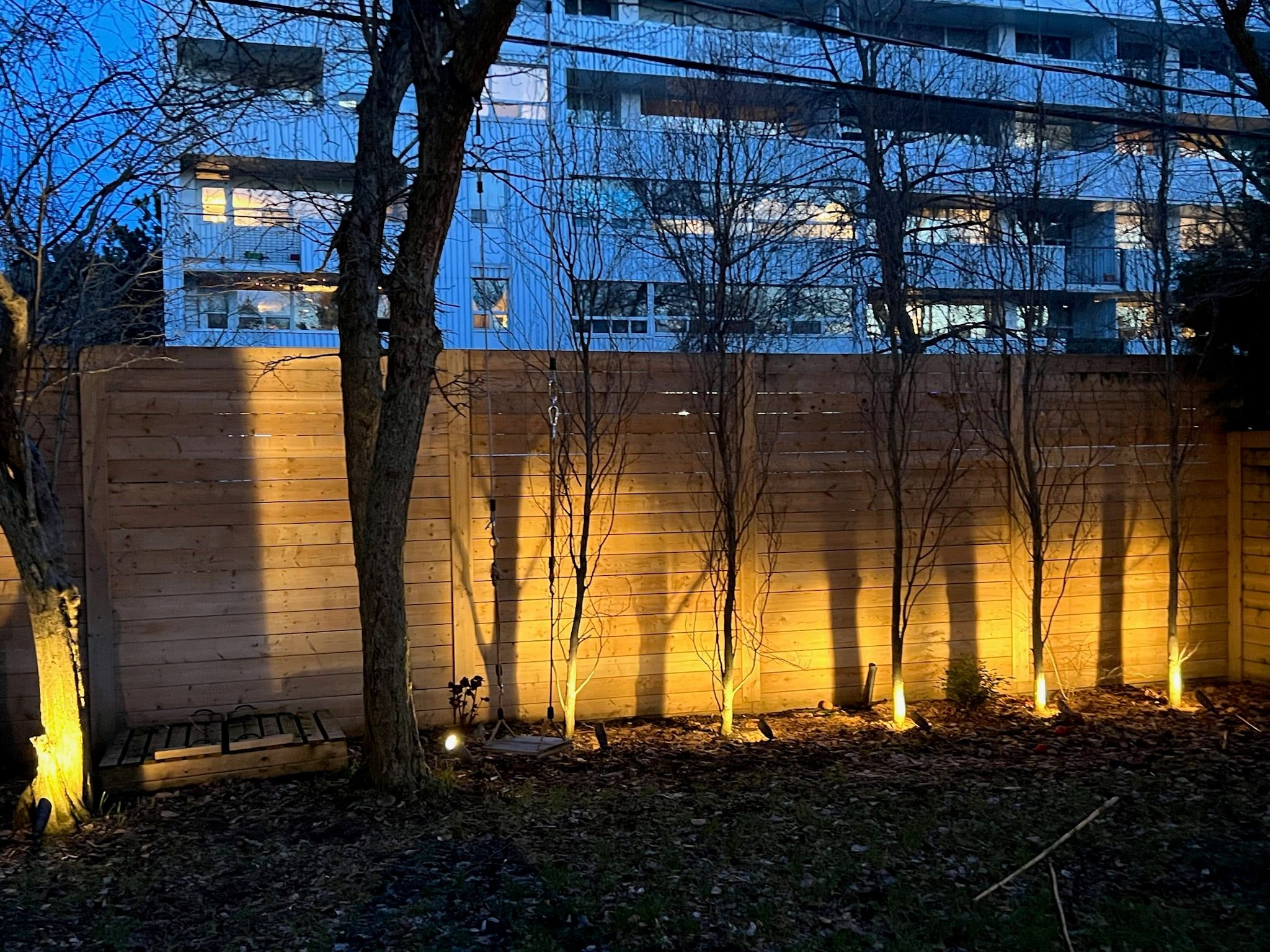 Uplights along a light wood garden fence at dusk.