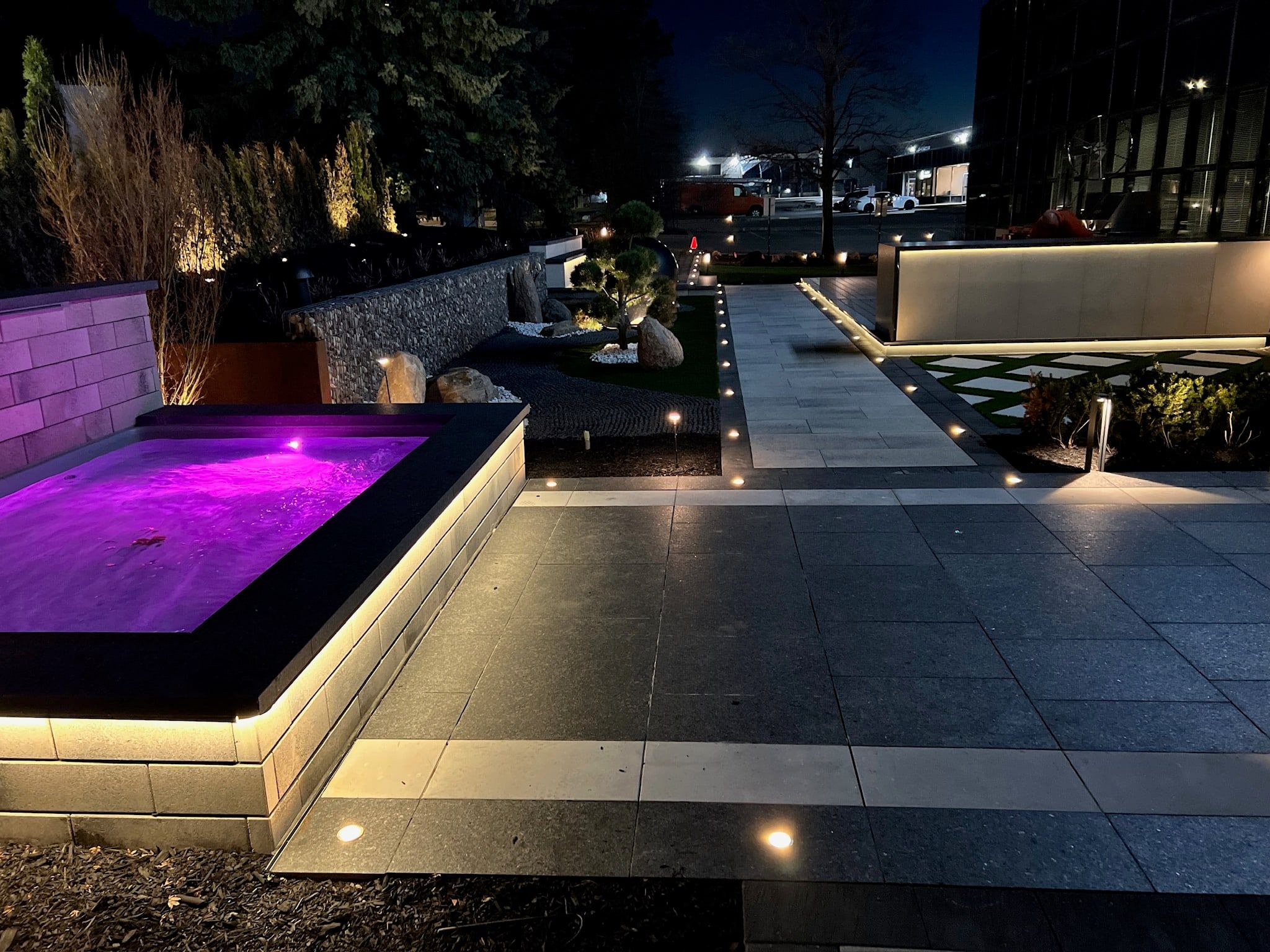 A spa glowing purple beside a lit terrace and walkway.