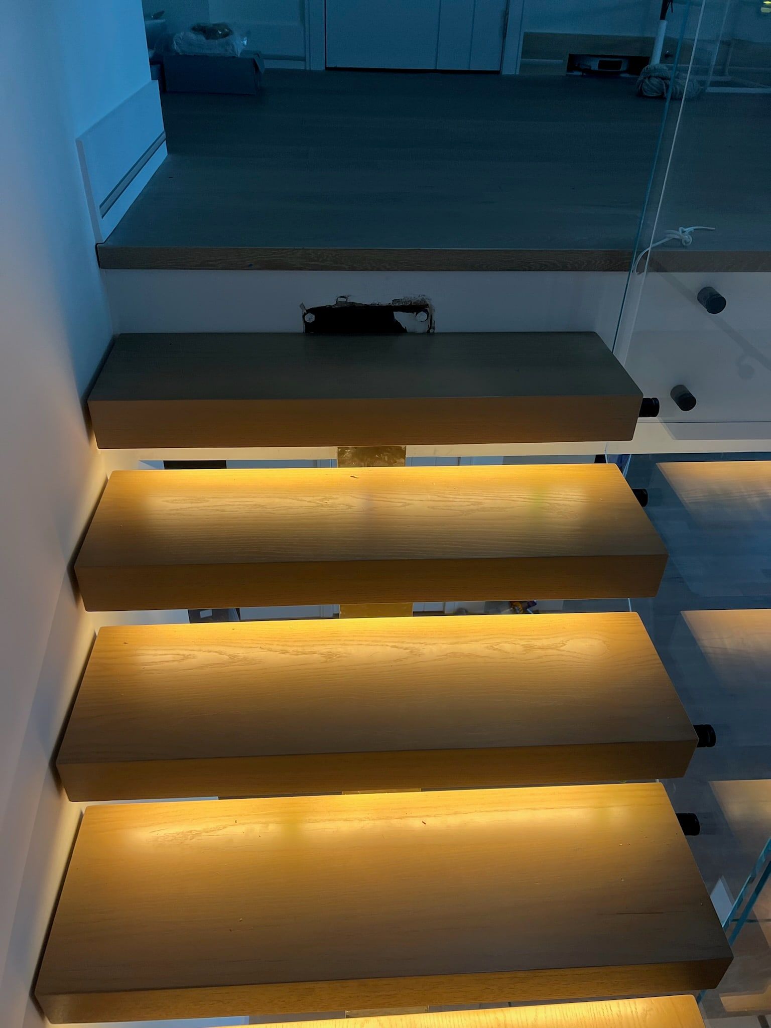 Close view of lit treads beside a frameless glass balustrade.