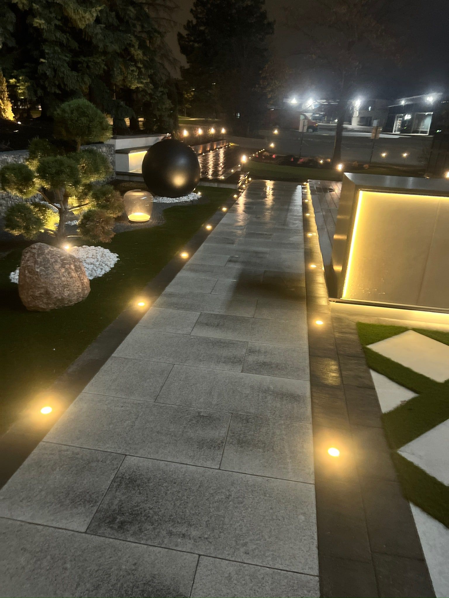 A long porcelain walkway lined with recessed lights and a lit planter wall.