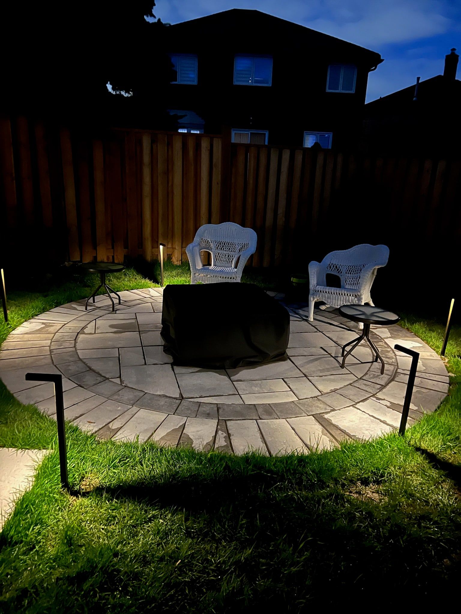 The round paver patio with path lights at its edge.