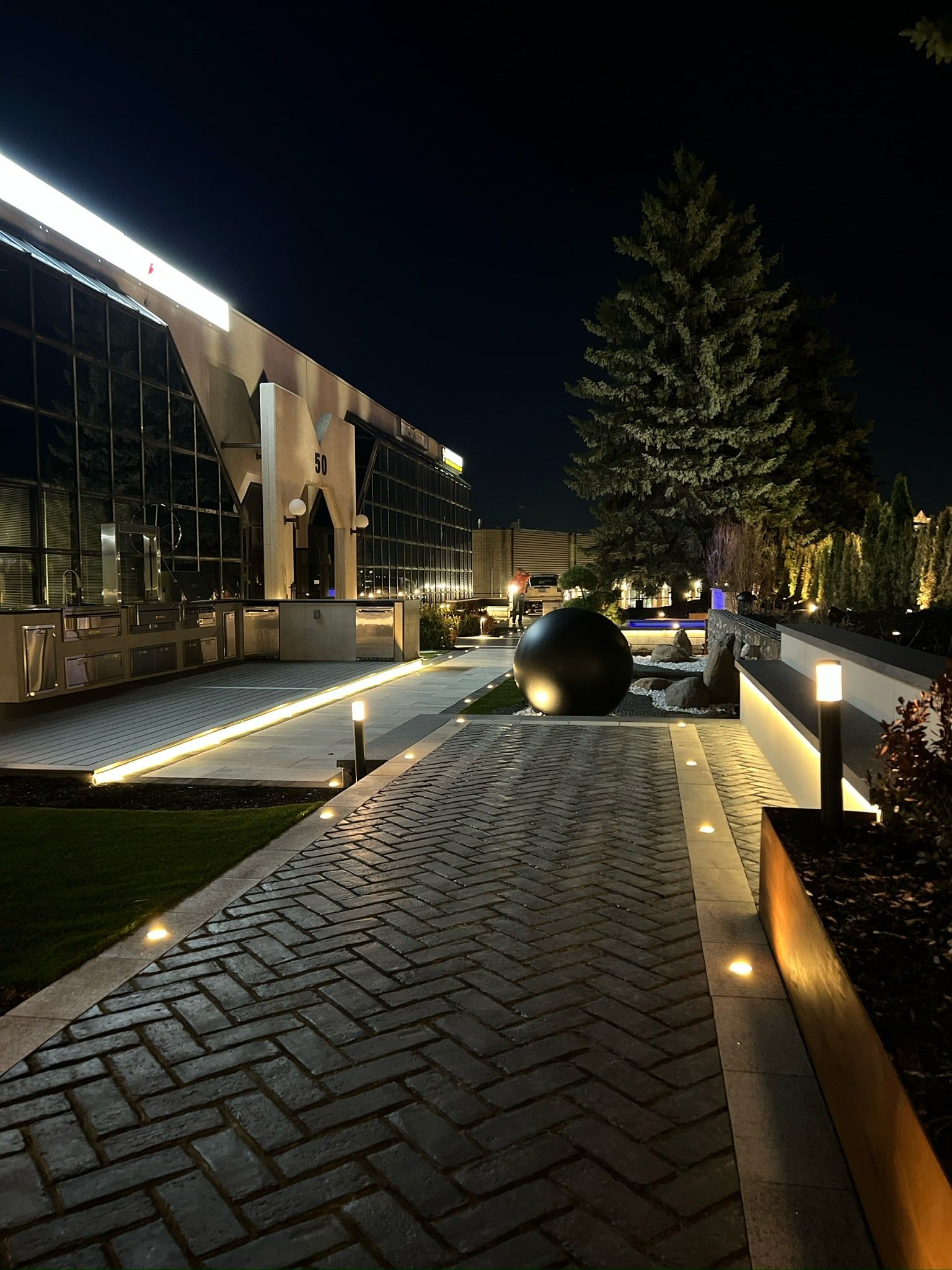 A herringbone walkway with recessed lights and a dark sphere sculpture.